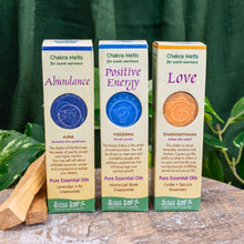 Load image into Gallery viewer, "Three packs of Aloha Bay Chakra Wax Melts on a wooden plank with green foliage in the background," - Down to Earth.