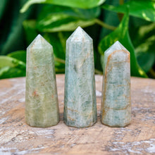 Load image into Gallery viewer, "Three Aquamarine Towers on a wooden base with green foliage in the background. This crystal is widely used in the metaphysical community to soothe anxiety," - Down to Earth.