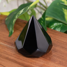 Load image into Gallery viewer, "Black Obsidian Chakra Extractor geometric crystal on a wooden plank with green foliage in the background," - Down to Earth.