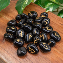 Load image into Gallery viewer, "Black Obsidian Rune Set on a wooden plank with green foliage in the background," - Down to Earth.