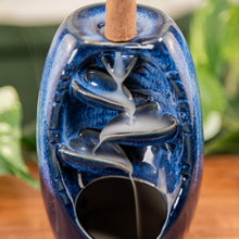Load image into Gallery viewer, "Close-up of the smoke streaming down a Blue Ceramic Backflow Burner on a wooden surface with green foliage in the background," - Down to Earth.