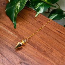Load image into Gallery viewer, "Brass Spike Pendulum on a wooden platform with green foliage in the background," - Down to Earth.