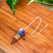 Load image into Gallery viewer, "Colorful crystal pendant on a silver chain on a wooden surface with green leaves in the background," - Down to Earth.
