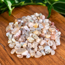 Load image into Gallery viewer, "Close-up of Flower Agate Crystal Chips on a wooden base with green foliage in the background," - Down to Earth.