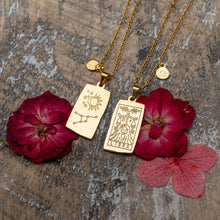 Load image into Gallery viewer, "Two Zodiac Necklaces in gold next to red flowers," - Down to Earth.