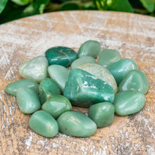 Load image into Gallery viewer, "Pile of tumbled Green Aventurine on a wooden plank with green foliage in the background," - Down to Earth.
