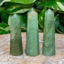 Load image into Gallery viewer, "Three Green Aventurine Towers on a wooden base with green foliage in the background," - Down to Earth.