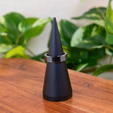 Load image into Gallery viewer, "Black cone-shaped object with a Hematite ring on a wooden surface with green plants in the background," - Down to Earth.