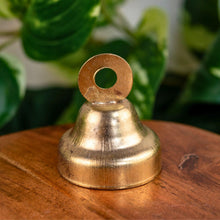 Load image into Gallery viewer, "Single iron hand bell on a wooden surface with green foliage in the background," - Down to Earth.