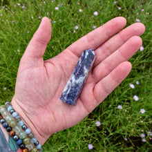 Load image into Gallery viewer, "Open palm with a Lepidolite tower in the center and greenery in the background," - Down to Earth.