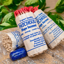 Load image into Gallery viewer, "Three rolls of patchouli rope incense with blue labels on a wooden surface with green foliage in the background," - Down to Earth.