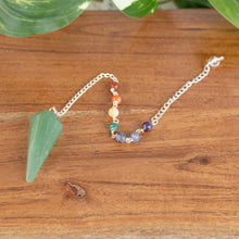 Load image into Gallery viewer, Premiere Green Aventurine Faceted Pendulum with 7 Chakra angled with plants on a styled background - Down To Earth