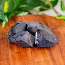Load image into Gallery viewer, Raw blue goldstone on a wooden surface with green leaves in the background