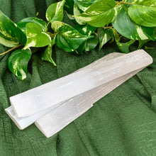 Load image into Gallery viewer, "Three large Selenite wands on a green cloth with foliage in the background," - Down to Earth.