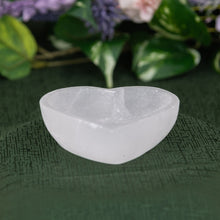 Load image into Gallery viewer, Selenite Heart-shaped Bowl on a green fabric background with blurred purple flowers in the background front - Down to Earth