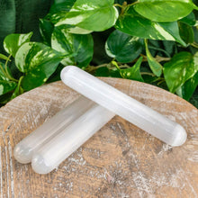 Load image into Gallery viewer, "Three Selenite Massage Wands on a wooden plank with green foliage in the background," - Down to Earth.