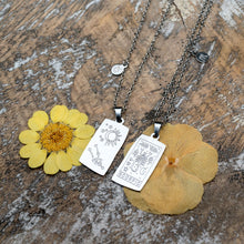 Load image into Gallery viewer, "Silver Zodiac Necklaces next to yellow flowers," - Down to Earth.