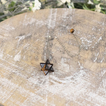 Load image into Gallery viewer, Tiger's Eye Merkaba Pendulum angled top down with plants displayed on a styled background - Down To Earth