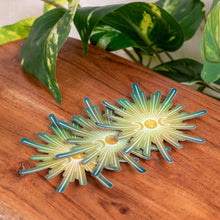 Load image into Gallery viewer, "Three Triple Moon Crystal Holographic Stickers splayed out on a wooden plank with green foliage in the background," - Down to Earth.