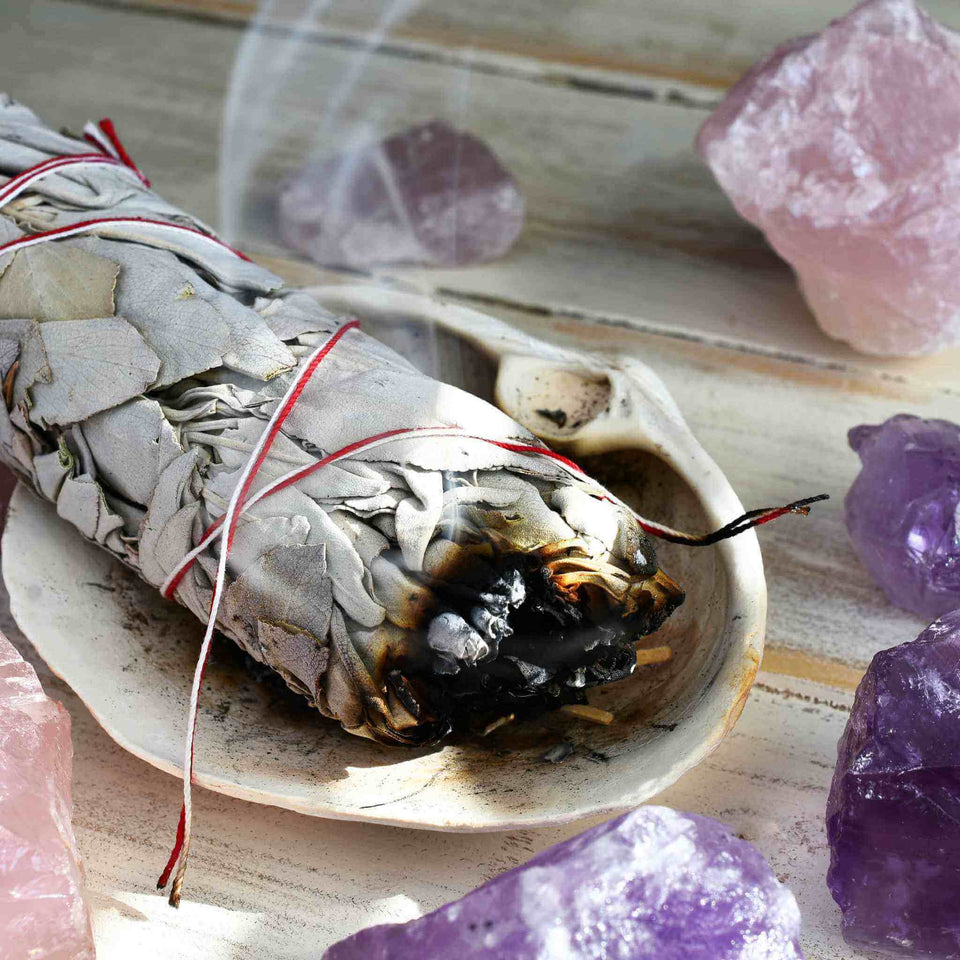 Burning White Sage Laying Inside an Abalone Shell with Amethyst and Rose Quartz Around it