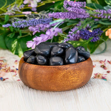 Load image into Gallery viewer, "Wooden bowl overflowing with pieces of tumbled black tourmaline with a floral background," - Down to Earth.