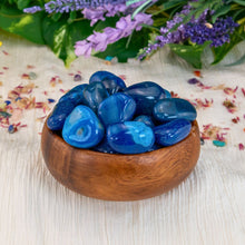 Load image into Gallery viewer, "Pieces of tumbled blue agate in a wooden bowl with a greenery background," - Down to Earth.