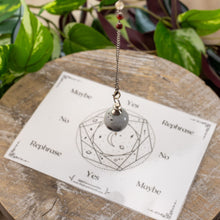 Load image into Gallery viewer, Photo of a moonstone pendulum hovering above a divination card. - Down to Earth.