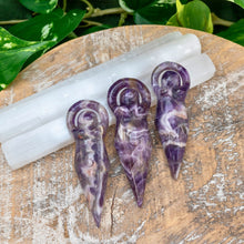 Load image into Gallery viewer, "Three Amethyst Goddess Statues leaning on selenite wands with green foliage in the background," - Down to Earth.