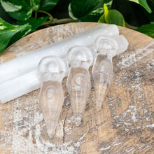 Load image into Gallery viewer, "Three Clear Quartz Goddess Statues leaning on Selenite wands with green foliage in the background," - Down to Earth.