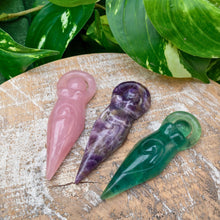 Load image into Gallery viewer, "Three Goddess Statues in the variations rose quartz, amethyst, and fluorite, on a wooden circle with green foliage in the background," - Down to Earth.