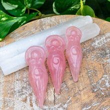 Load image into Gallery viewer, "Rose Quartz Goddess Statues leaning on Selenite wands with green foliage in the background," - Down to Earth.