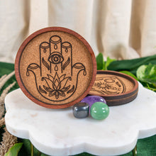 Load image into Gallery viewer, "Wooden coaster with Hamsa design on a marble surface with crystals and leaves," - Down to Earth.