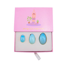 Load image into Gallery viewer, "Top-down view of an ajar opalite yoni egg set in a light pink box with a graphic of a woman practicing yoga," - Down to Earth.