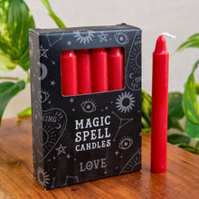 Load image into Gallery viewer, "Box of red 'Magic Spell Candles Love' with a single candle on a wooden surface with plants in the background," - Down to Earth.