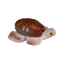 Load image into Gallery viewer, "Right side of a stone-carved figurine in the shape of a sea turtle with yellow eyes against a white background," - Down to Earth.