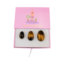 Load image into Gallery viewer, "Top-down view of an open tiger's eye yoni egg set with a graphic of a woman practicing yoga on the lid," - Down to Earth.