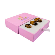 Load image into Gallery viewer, "Left-side view of an ajar yoni set, showcasing three tiger's eye yoni eggs within a light pink box," - Down to Earth.