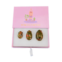 Load image into Gallery viewer, "Top-down view of three unakite yoni eggs in a light pink box with a graphic of a woman practicing yoga on it," - Down to Earth.
