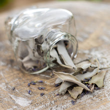 Load image into Gallery viewer, A heart-shaped bottle with dried lavender and white sage spills out, revealing a closer look at the herbs. - Down to Earth.