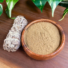 Load image into Gallery viewer, "Wooden bowl with green powder, sage bundle, and leaves on a wooden surface," - Down to Earth.
