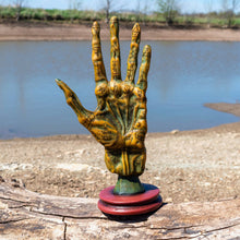 Load image into Gallery viewer, "Decorative hand sculpture with text on a wooden log by a water body," - Down to Earth.
