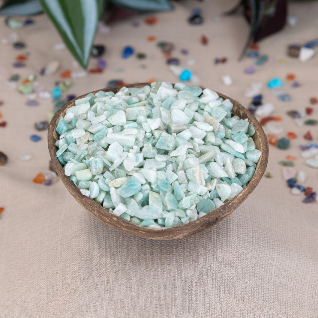 Small wooden bowl filled with Amazonite Crystal Chips on a beige surface with scattered stones around - Down To Earth