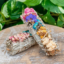 Load image into Gallery viewer, "Sage bundle with assorted colored flowers on a wooden plank with green foliage in the background," - Down to Earth.
