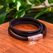 Load image into Gallery viewer, "Black Leather Wrap Bracelet on a wooden plank with green foliage in the background," - Down to Earth.

