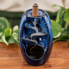 Load image into Gallery viewer, "Blue Ceramic Backflow Burner with a lit incense cone on top with the smoke flowing down the piece with green foliage in the background," - Down to Earth.
