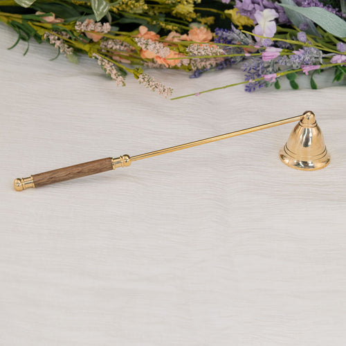 Brass Candle Snuffer on white cloth with flowers in the foreground - Down To Earth