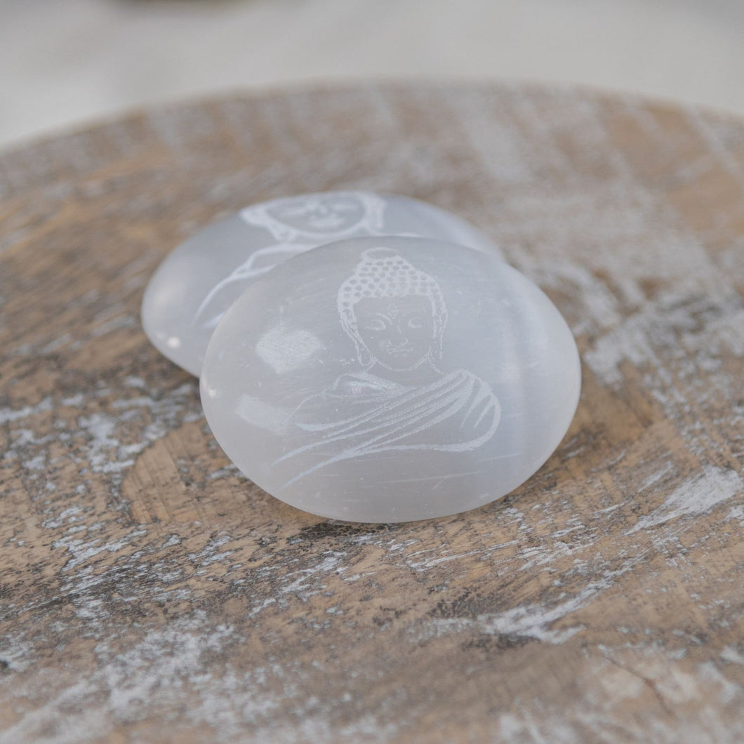 Buddha Engraved Selenite Palm Stones on a wooden surface - Down to Earth 