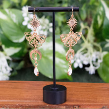 Load image into Gallery viewer, Celestial Sun &amp; Moon Butterfly Earrings in stand displayed on a styled background - Down To Earth
