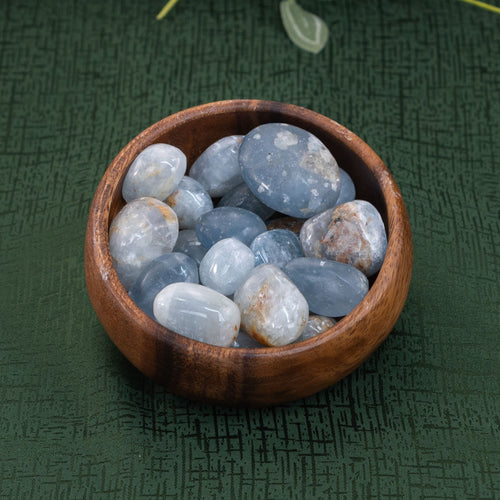 Tumbled Celestite crystals in a wooden bowl on a green cloth - Down to Earth