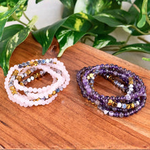 Load image into Gallery viewer, "Two sets of beaded bracelets on a wooden surface with green leaves in the background," - Down to Earth.
